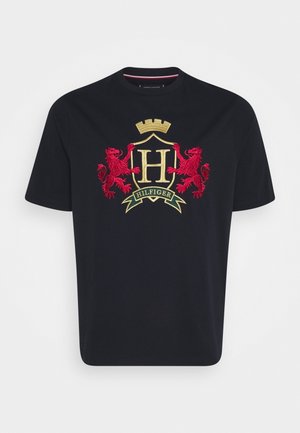 Czarna bawełniana koszulka z dużą haftowaną godłem w złotym i czerwonym kolorze, z dwoma lwami, koroną i literą 'H' na środku.