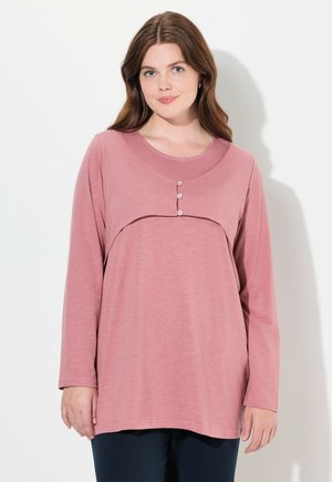 Langärmliges Oberteil aus weichem rosa Stoff, mit rundem Halsausschnitt und einem mehrlagigen Design, das drei dekorative Knöpfe im Brustbereich aufweist.