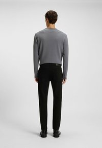 Camisa de manga larga gris con textura acanalada combinada con pantalones negros de pierna recta y botas negras, vista desde atrás. Diseño sencillo sin patrones notables.