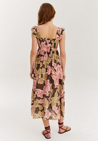 Maxi šaty s kvetinovým vzorom v ružovej, zelenej a hnedej farbe. Majú elastický chrbát a volánové rukávy. Nosia sa s plochými sandálmi na remienky.