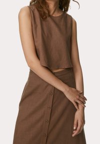 Top corto marrón en un tejido ligero y suave, combinado con una falda a juego que presenta un cierre de botones en la parte delantera. Diseño sin mangas.