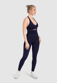 Mørkeblå sports-bh med udskæringsdetalje, kombineret med matchende høj-taljede leggings. Glat stof, tætsiddende design og elastisk tekstur.