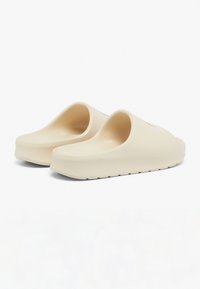 Beige closed-back clogs with smooth, matte finish, rounded toe, and thick sole; features ribbed tread for traction.
