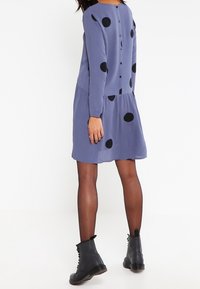 Sinine pikade varrukatega kleit mustade täppidega ja nööpidega. Laienev seelik sujuva tekstuuriga, koos mustade pitsitud saapatega.