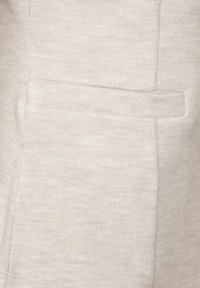 Tissu beige clair avec une fine texture côtelée. Dispose d'une poche discrète sur le côté, de coutures détaillées et d'une surface lisse.
