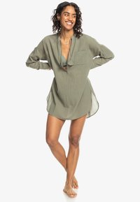 Vestito camicia verde oliva con colletto, maniche lunghe, tasca sul petto e spacco laterale. Realizzato in tessuto leggero e textured.