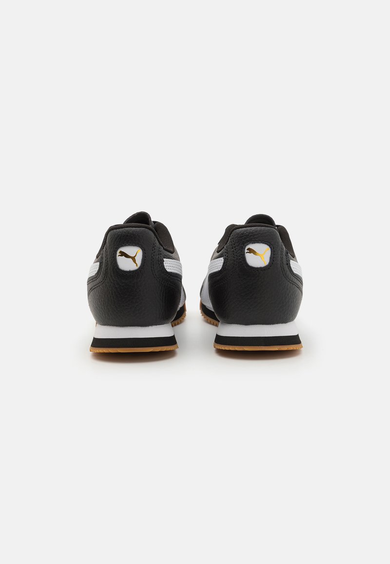 Baskets de sport en cuir noir avec des accents blancs et gris, bout rond, semelle en caoutchouc et détail de logo doré sur le talon.