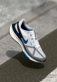 Hvit Nike løpesko med blå aksenter, stripet tekstur, lissesystem og svart hælstøtte. Lettvektsdesign for ytelse.
