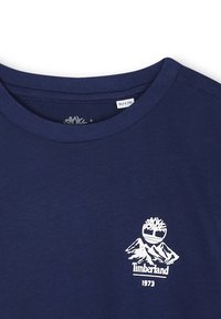 Marineblauw T-shirt met ronde hals en wit Timberland-logo met een boom en bergen, en het jaar 1973 eronder gedrukt.