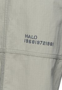 Ljust grått tyg med ett rutmönster, med marinblå text "HALO 196819721981" på en sida, med en slät yta och sydda kanter.