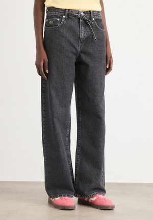 Black straight-leg jeans with a high waist, front pockets, and a button fly. Paired with pink sneakers featuring a zigzag pattern.