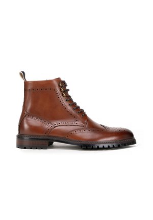 Brązowy skórzany botek sięgający kostki z detalami w stylu brogue, okrągłym noskiem i czarną gumową podeszwą z wyżłobieniami. Wyposażony w metalowe oczka oraz zapięcie na sznurówki.