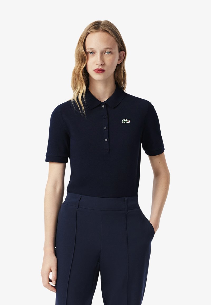 Granatowa koszulka polo wykonana z miękkiego materiału, z kołnierzykiem, krótkimi rękawami i zielonym haftowanym logo po lewej stronie klatki piersiowej. Dopasowany krój.