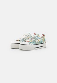 Witte sneakers met een dikke zool, voorzien van een tropisch bloemenpatroon in groen, geel en rood. Zwarte strepen aan de zijkant van de zool.