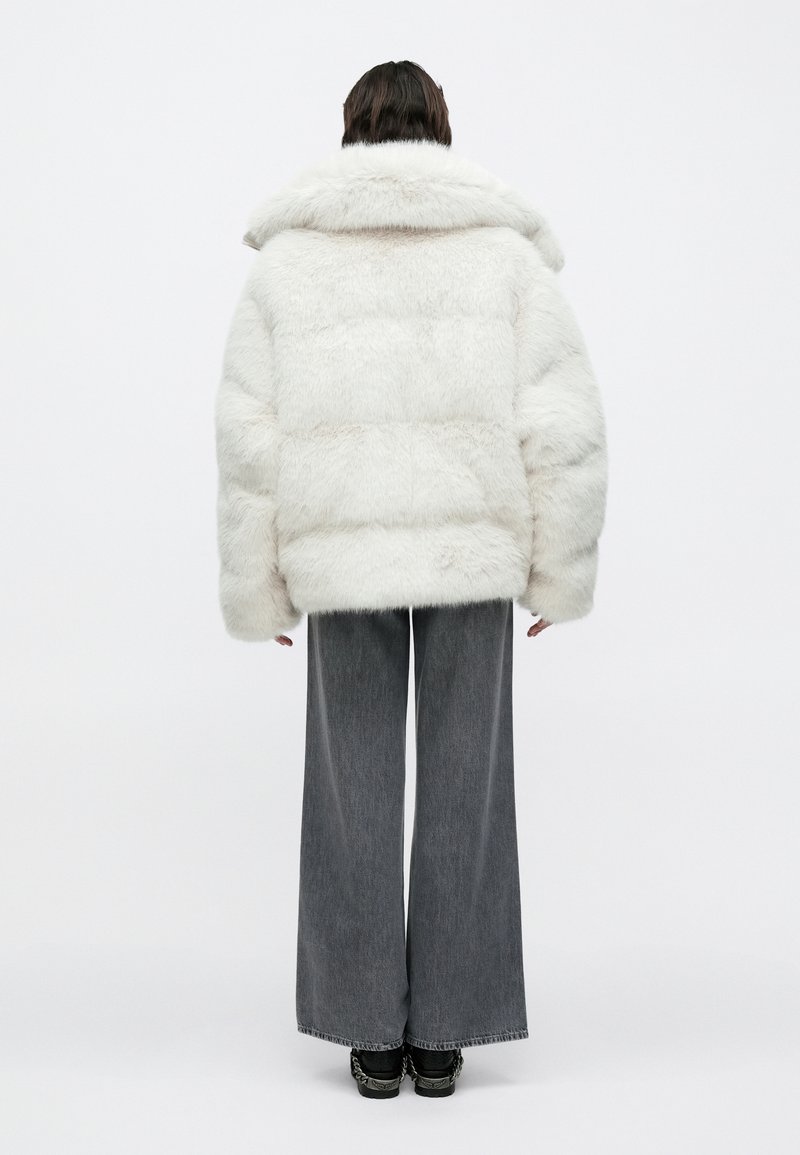 Veste matelassée en fausse fourrure blanche avec un large col, une texture épaisse et une forme carrée, associée à un pantalon en jean gris ample et des chaussures noires.