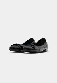 Paire de mocassins noirs en cuir brillant sans lacets avec bouts carrés arrondis et petits talons sur fond clair uni.