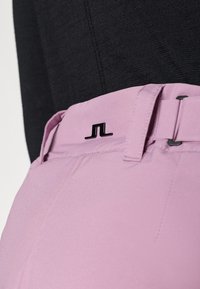 Lichtroze broek met een gladde textuur, voorzien van een zwart logo op de tailleband en een veilige riemlusse ontwerp.