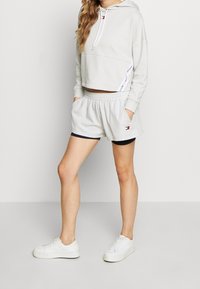 Sudadera corta gris claro y pantalones cortos a juego con cintura elástica. Zapatillas blancas con suela texturizada complementan el conjunto.