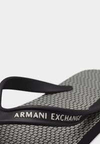Μαύρο και άσπρο σαγιονάρι Armani Exchange με σχεδιασμένο πέλμα και λουράκι με λογότυπο σε κοντινή όψη.