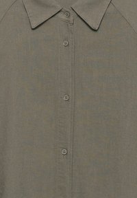 Gros plan sur le devant d'une chemise vert olive avec col et cinq boutons visibles le long du patte centrale.