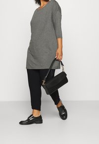 Grijze tuniek top met driekwartmouwen, gecombineerd met marineblauwe broeken. Een zwarte handtas en glanzende zwarte schoenen maken de look compleet.