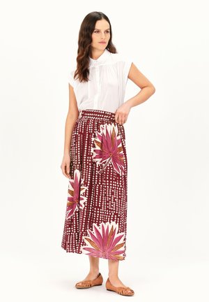 Blouse blanche à boutons, associée à une longue jupe bordeaux avec de grands motifs floraux roses et blancs ainsi que des motifs circulaires.