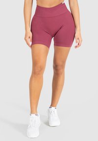 Burgundské šortky s vysokým pasem vyrobené z elastického materiálu, s ribovaným designem a hladkou texturou, doplněné o bílé sportovní tenisky.