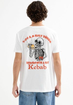 Camiseta de manga corta blanca con un gráfico de un esqueleto sosteniendo comida, con texto en naranja y negro, y un corte relajado.