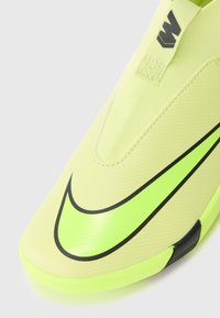 Zapatilla deportiva de color amarillo neón con un diseño elegante, superficie texturizada y un prominente logo de Nike en color negro. Cuenta con una tirador en el talón.