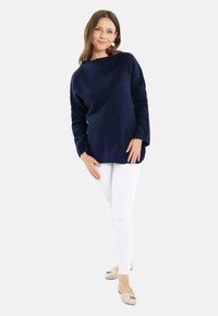 Maglione blu navy lavorato a maglia con un motivo testurizzato, abbinato a jeans skinny bianchi e ballerine beige con un accent decorativo.