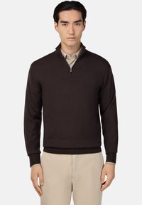 Brūns zip-up džemperis ar garām piedurknēm un ribotām aprocēm, nēsāts virs bēšas krekla ar apkakli. Gluda tekstūra, ikdienas piegriezums, minimālistisks dizains.