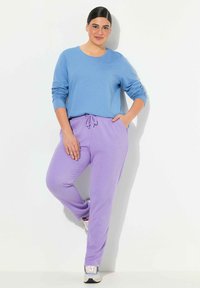 Ljust blå långärmad skjorta i kombination med lila dragstringbyxor av sweatpants, med elastiska muddar och fickor. Outfiten är avslappnad och bekväm.