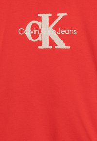 Röd bomullst-shirt med en texturerad vit broderad logotyp med "Calvin Klein Jeans" under den stora stiliserade "CK."