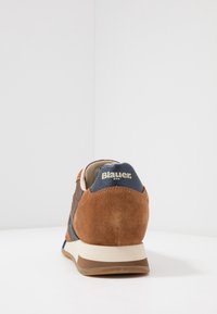 Baskets en daim marron avec des accents bleu marine, dotées d'une semelle de couleur crème et d'un logo sur le talon. Construites avec des matériaux texturés.