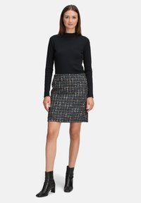 Schwarzes, tailliertes Langarmoberteil, kombiniert mit einem bunten Tweed-Minirock. Der Rock besteht aus blauen, weißen und schwarzen Fäden. Schwarze Stiefeletten.
