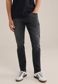 Tamne traperice u tamno sivoj boji, uskog kroja. Imaju klasičan dizajn s pet džepova, suptilno izbleđivanje i mekani materijal. Nosi se s bijelim tenisicama.