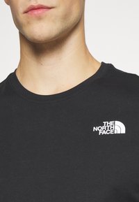 Czarna bawełniana koszulka z okrągłym dekoltem, z małym białym logo "The North Face" na lewej stronie klatki piersiowej.