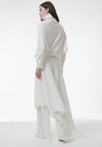 Witte gebreide trui met hoge kraag, gecombineerd met een vloeiende witte rok met een asymmetrische zoom en een zachte textuur.