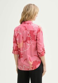 Pink floral shirt featuring roll-up sleeves, button detail, and a round hem with white and darker pink floral patterns on the fabric.