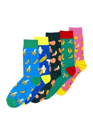 Nogi skrzyżowane, w niebieskich skarpetkach z zielonym mankietem i palcami, z wzorem obieranych i całych żółtych bananów.