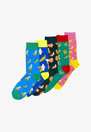 Ben krydset iført blå sokker med grønne manchetter og tæer, mønstret med skrællede og hele gule bananer.