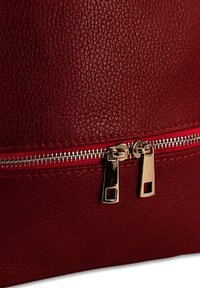 Surface en cuir texturé rouge avec une fermeture éclair horizontale dotée de deux tirettes en métal argenté.