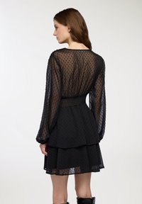 Abito nero con tessuto trasparente a pois, maniche lunghe e gonna a strati. Presenta una vita arricciata e una texture sottile.