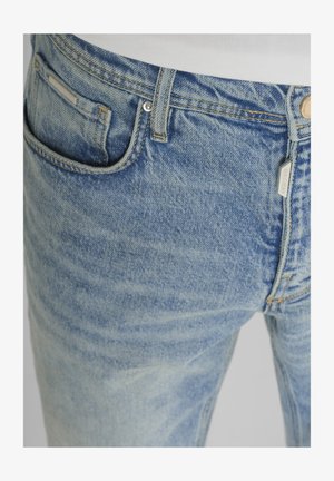 Lichtblauwe denim jeans close-up met voorkantzak, ceintuurlus, knoop en zichtbare stiksel details.
