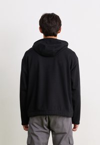 Sudadera con capucha negra de corte relajado, con una textura suave y puños acanalados, combinada con pantalones cargo grises.