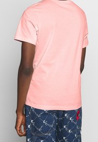 T-shirt di cotone rosa chiaro con maniche corte, scollo rotondo e una consistenza liscia, abbinata a pantaloni corti blu a fantasia.