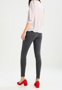 Blusa grigia chiara, semi-trasparente, con maniche a sbuffo; abbinata a jeans skinny grigi scuri. Tacchi in camoscio rossi completano l'outfit.