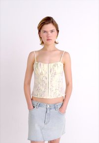 Corsage floral jaune avec des bretelles fines et des plis verticaux, associé à une jupe en denim bleu clair, dotée de poches avant et d'une fermeture à boutons.