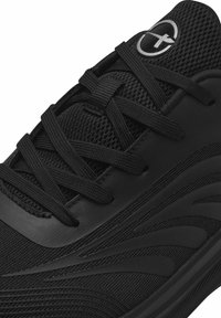 Black athletic shoe featuring a textured mesh upper, flat laces, and a smooth rubber sole with a wavy pattern on the side.