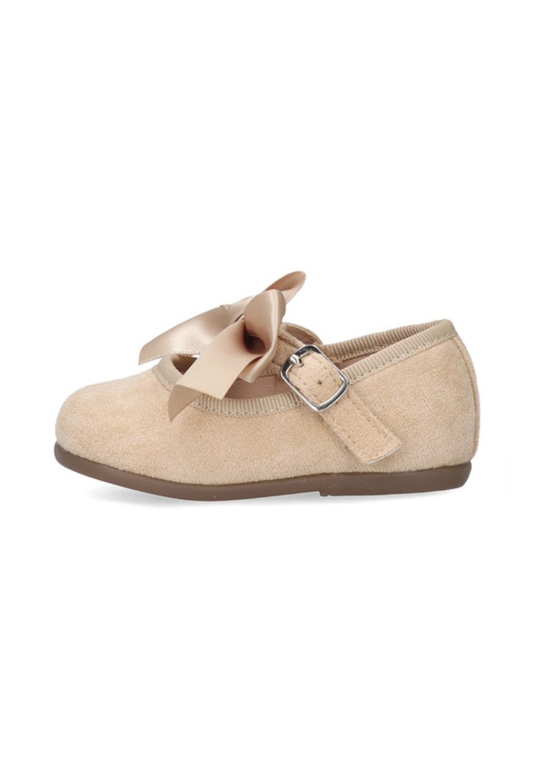 Zapato Mary Jane de gamuza beige con lazo de satén, correa con hebilla ajustable y suela plana marrón, diseñado para niños pequeños o jóvenes.